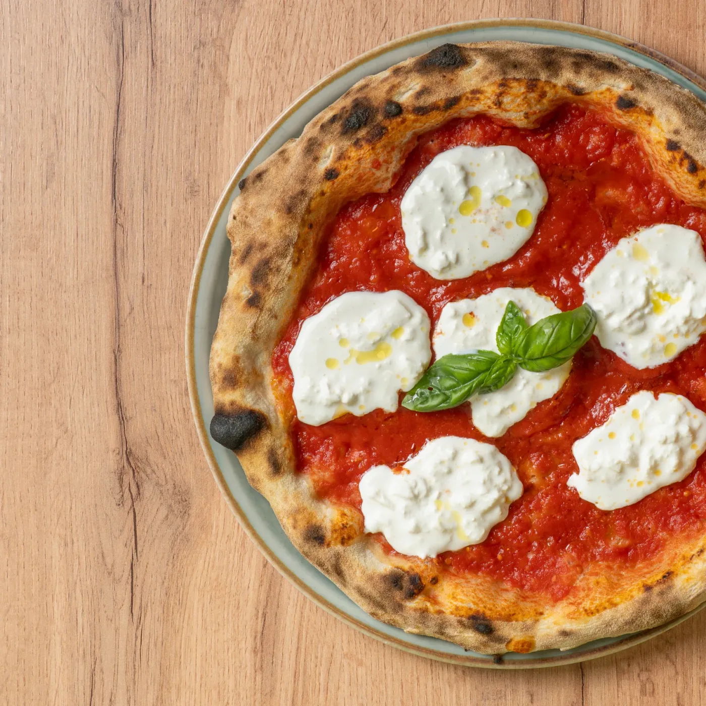 Una pizza con pomodoro, stracciatella di burrata e basilico fotografata dall'alto su un tavolo di legno