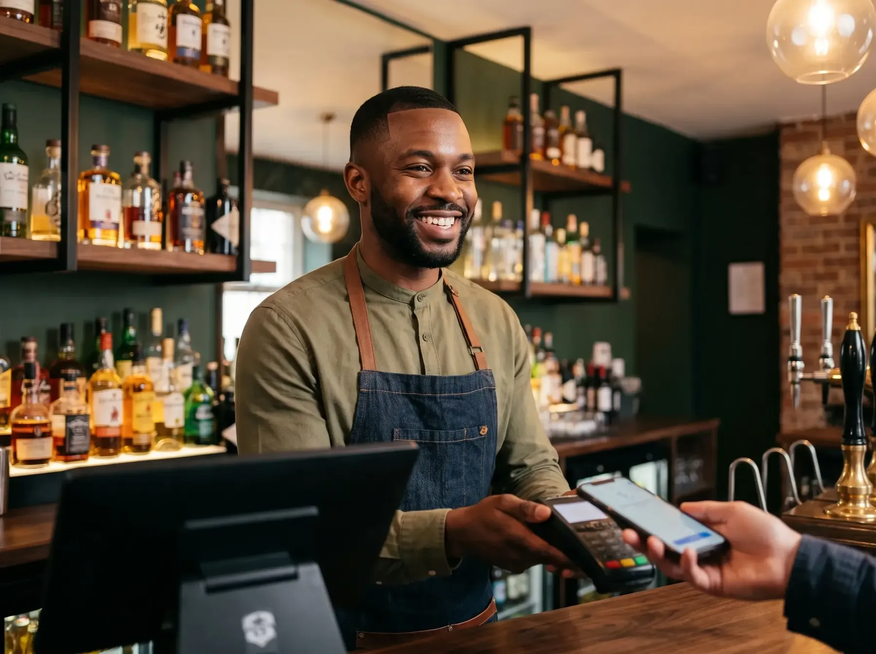 Barista sorridente che incassa un pagamento con il telefono al bancone di un pub